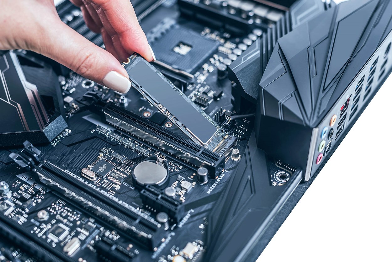 A close-up of a person installing an M.2 NVMe SSD onto a gaming motherboard, showcasing the PCIe slot and modern motherboard design.